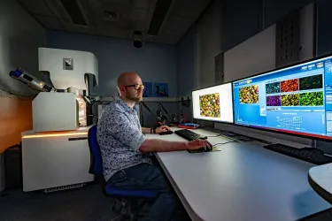 A technician works at computers displaying microscopic images, with a TESCAN electron microscope nearby.