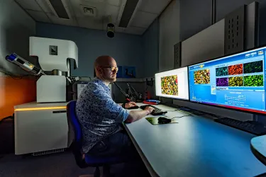 A scientist sits at a bank of computer screens performing scanning electron microscopy