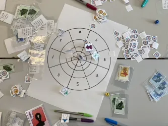 A tabletop game in progress showing cards, tokens and a target board used for exploring character, emotion and decision-making.