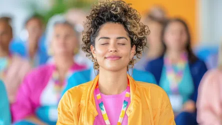 A person with curly hair and hoop earrings in a yellow jacket peacefully sitting with closed eyes.
