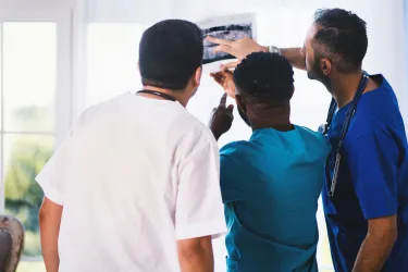 Three healthcare professionals examining an X-ray next to a window.