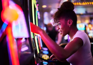 A woman playing a brightly lit slot machine in a casino.