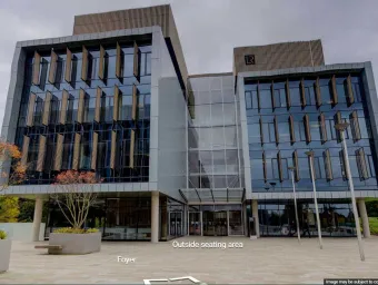 Large modern building on a concrete plaza, with a few trees.