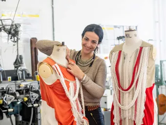 A student pins clothes and fabrics onto a mannequin.