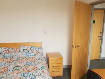 Bedroom with large double bed with floral sheets and a wooden nightstand.