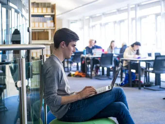 Student sitting with his laptop next to the windows in Waterfront Campus library.