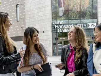 Four students sat talking and laughing in front of the John Hansard Gallery, part of the City Centre Campus