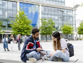 Students sat on bench talking in guildhall square, outside the 1GS Building.