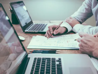Hands of two people shown in front of laptop and working together on written report