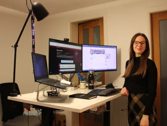 Elizabeth Gardiner standing for a photo next to a dual monitor computer set-up.