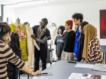 Fashion design tutor presenting a garment to a group of students in a studio.