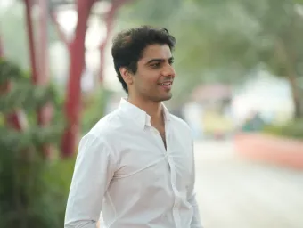 Law graduate and entrepreneur Rohit is standing looking to the right of the camera. There are out of focus trees and shrubs behind him.