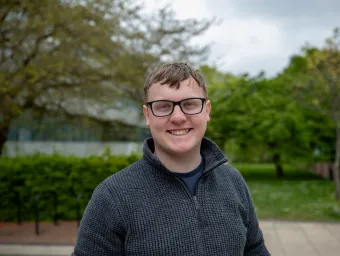 Smiling student wearing glasses standing outside the Physics building..
