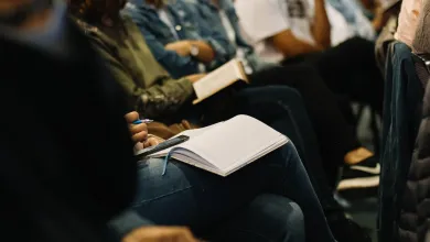 Looking along a row of people at a seminar. We can't see their faces. Some of them are taking notes.