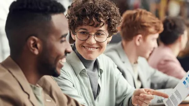 Two individuals smiling and reviewing a document together, with others in soft focus in the background, suggesting a collaborative work environment.