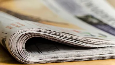 A rolled-up newspaper on a wooden surface, with visible pages and text.