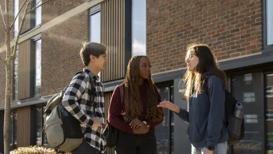 Three students chatting outside a university halls of residence. 
