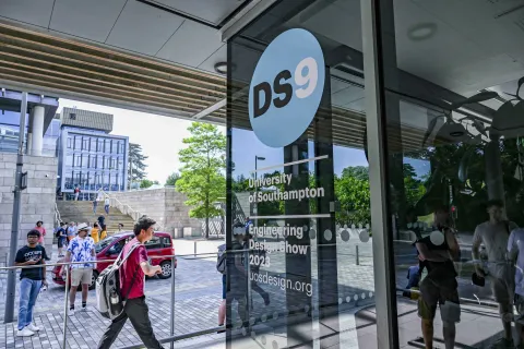 A picture of the Engineering Design Show 9 artwork "DS9" on the glass windows of an engineerin building, there are students walking past in the background.