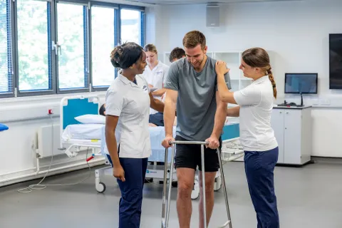 A patient, supported by 2 students, learns to walk using a walking frame.