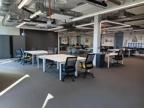 Modern open office space with white desks, black chairs, grey cabinets, and a collaborative area with murals.
