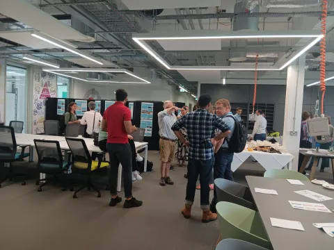 Modern office space with several people engaged in conversation around a table filled with refreshments. 