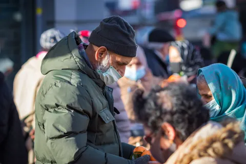 People wearing masks gather outdoors, some handing out fruit during a community food distribution.