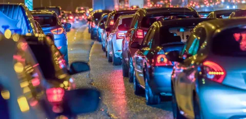 Looking along 2 rows of cars, bumper to tail with the rear lights shining. it is dark apart from the car lights.