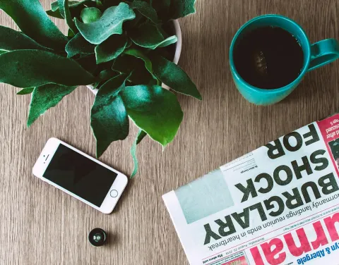 table with a mobile phone, plant, beverage in a mug and a newspaper