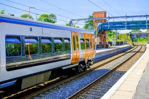 A modern passenger train pulling into a quiet railway station on a sunny day.