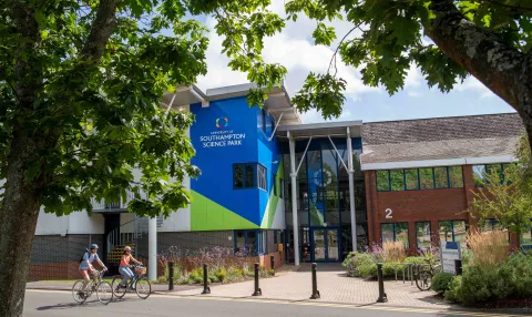 An exterior view of the main building at the Science Park. It is a sunny day and there are 2 cyclists on the road in front of the building.