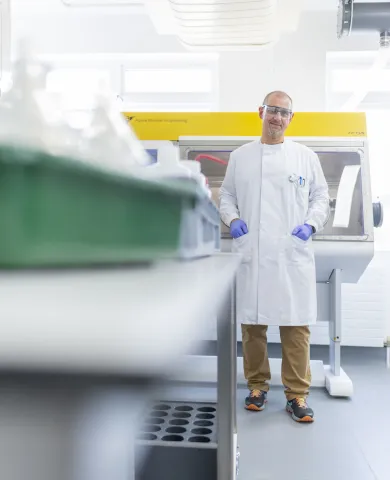 Person in a lab coat standing in a laboratory near a fume hood.
