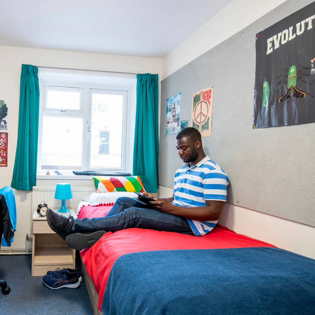 Student sat on bed, working on tablet computer.