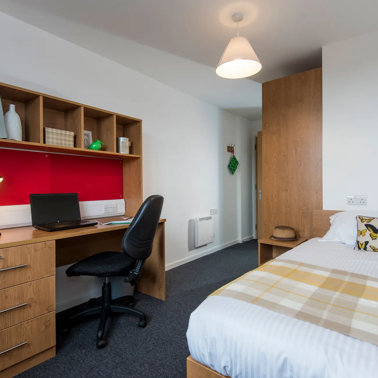 A modern student bedroom with white walls, wooden desk and neatly made double bed.