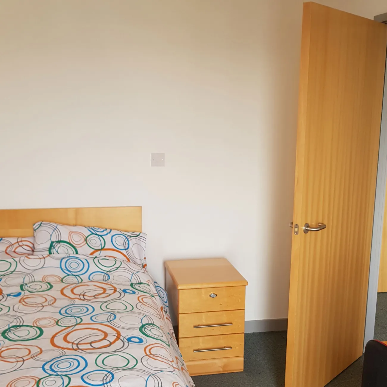 Bedroom with large double bed with floral sheets and a wooden nightstand.