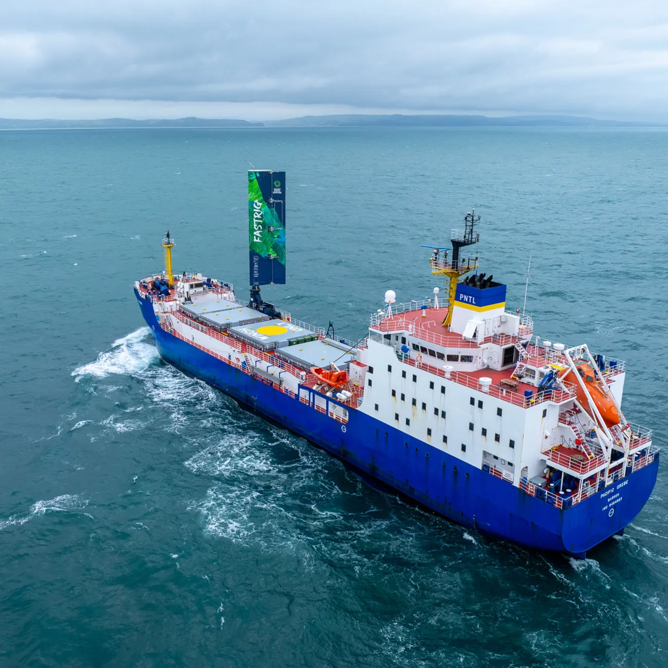 A large cargo vessel sailing on the ocean. It has a 20 metre-high wing sail.