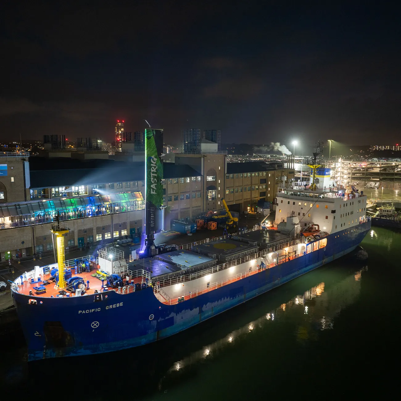 A large cargo vessel docked at the School of Ocean and Earth Science in Southampton. It's night and the vessel has a 20 metre-high wing-sail attached.