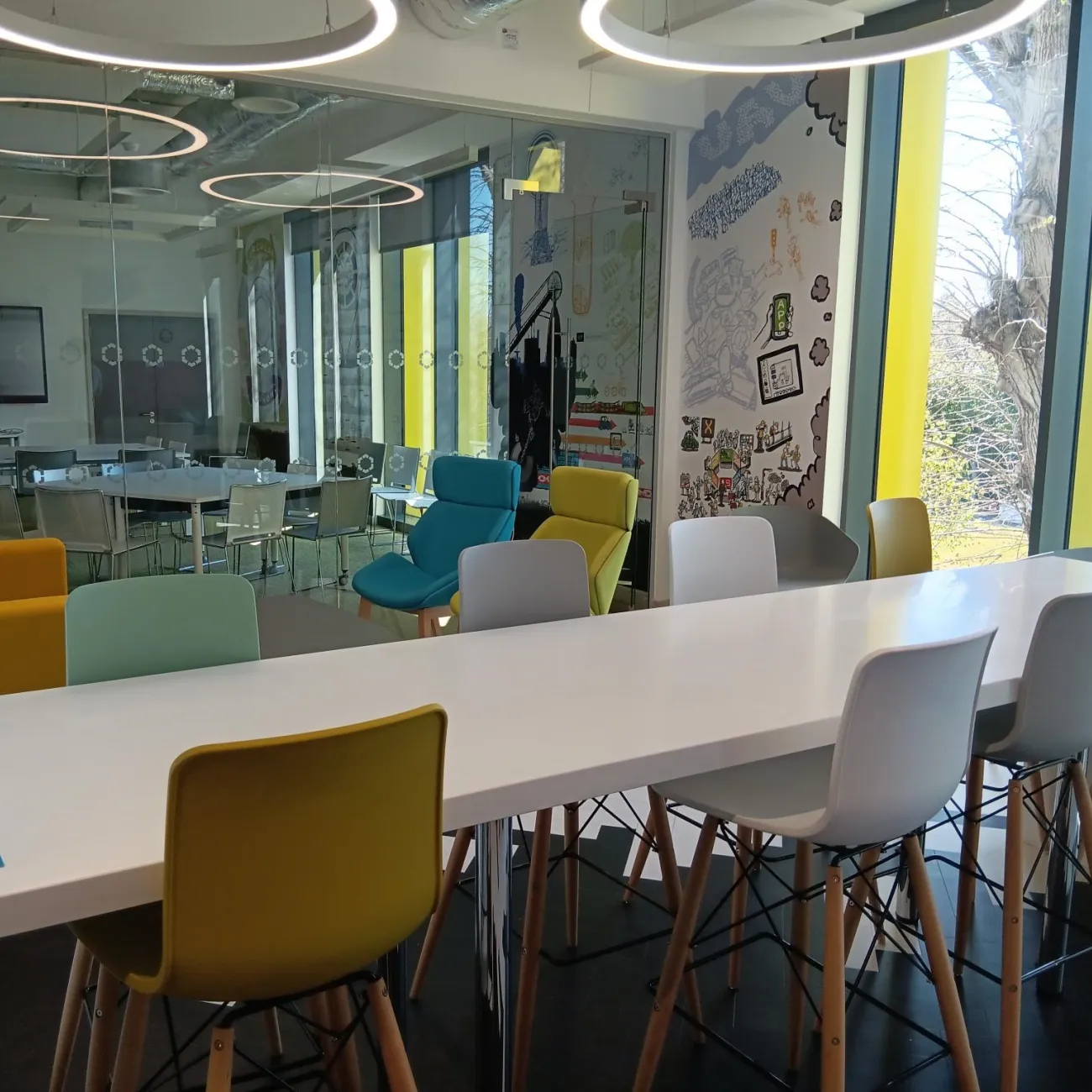 Modern meeting space with a white table, colourful chairs, and wall murals.