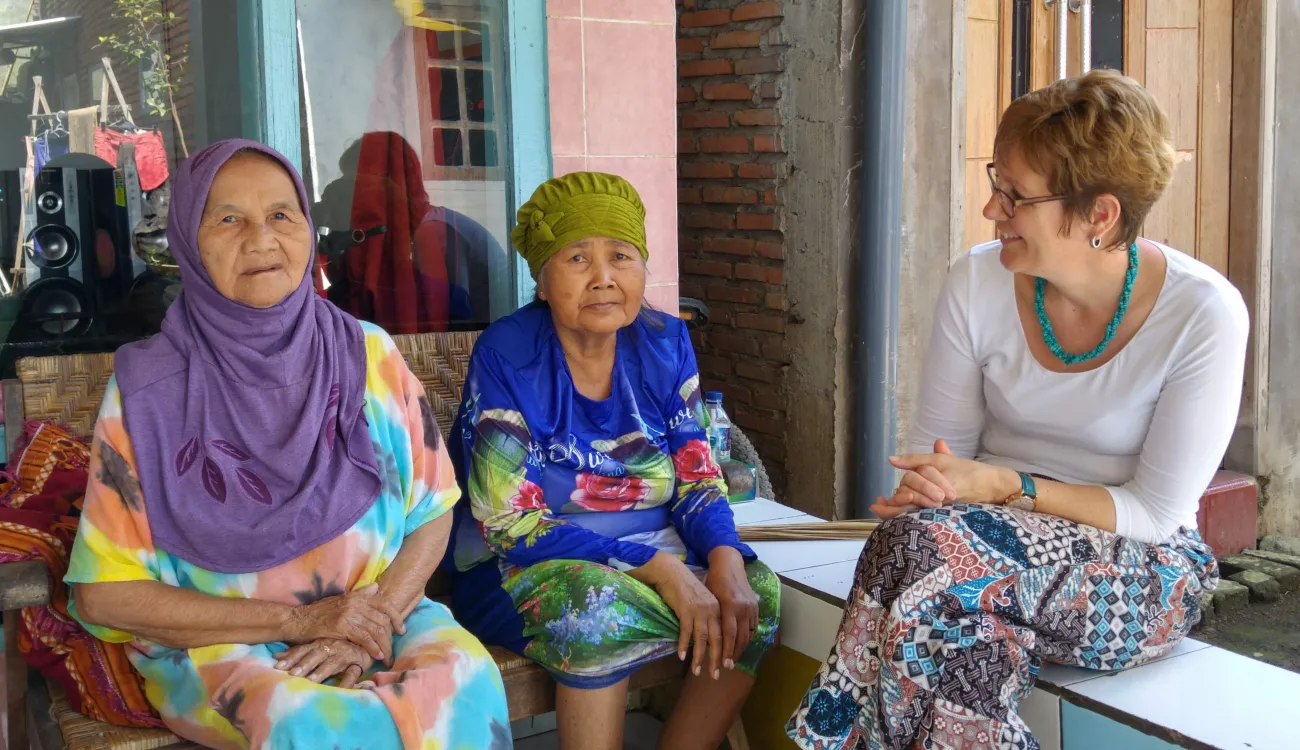Elisabeth Schroeder-Butterfill interviews two Indonesian women as part of her research. They are sitting on benches and smiling.