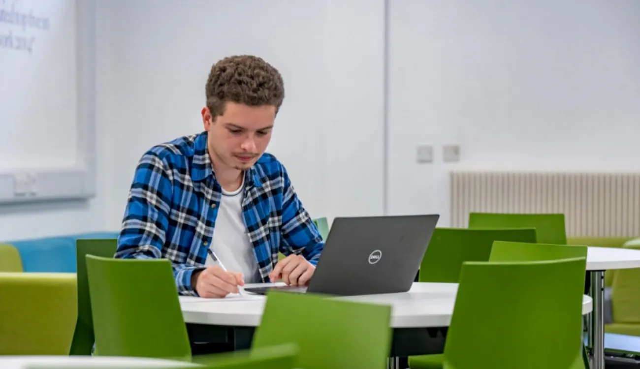 An undergraduate student studies in a dedicated quiet space with tables and brightly coloured seating