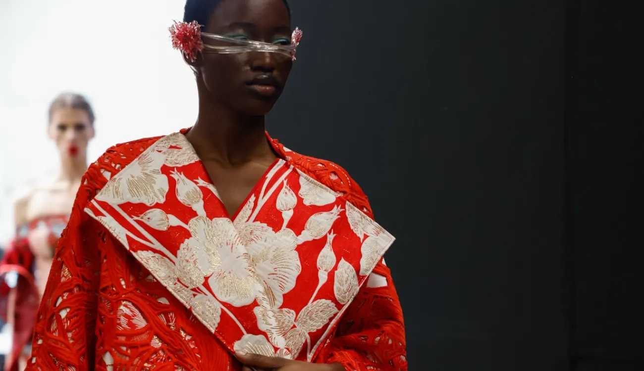 A catwalk model sports a dramatic red and white floral jacket with outsized lapels