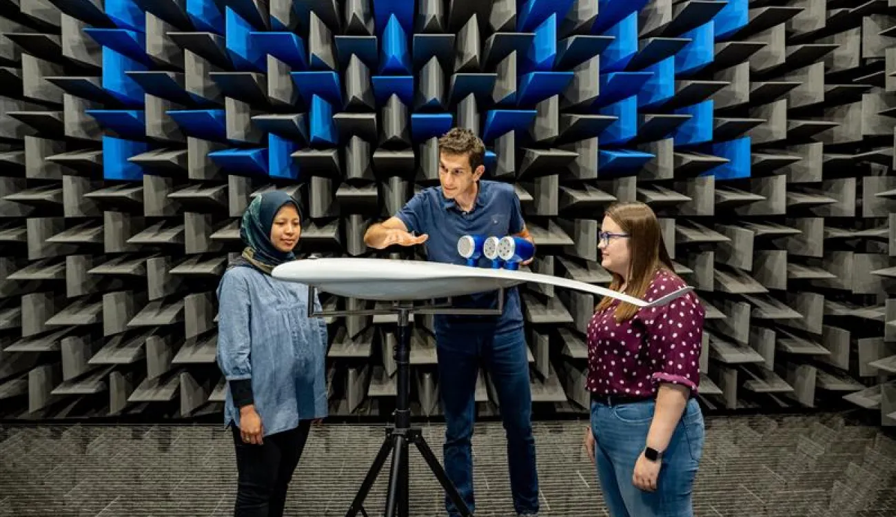 One man and two women are working together at an anechoic wind tunnel, testing a scale model of an aircraft.