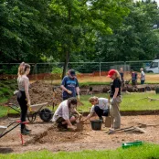 Archaeology students working at an excavation site with wheelbarrows and spades