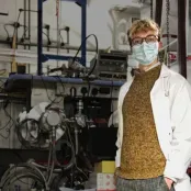 Engineering student Oliver Hitchens in a lab coat and mask in front of lab equipment