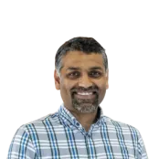 Professor Sumeet Mahajan wearing a check shirt and smiling at the camera against a white background
