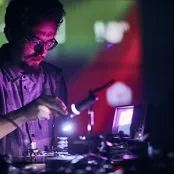 A man with glasses stands over equipment under purple and pink lighting.