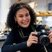 Head and shoulders portrait image of Amber Williams, BA Archaeology and Ancient History Year Abroad student, holding a camera and smiling at the camera.