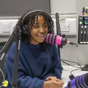 Olivia Coker, BA Film, TV and Digital Media student in a recording studio interviewing 2 other students. All 3 students have headphones on and a large microphone in front of them. 