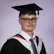 Head and shoulders graduation portrait image of Tommie Bloomfield, MSc Archaeology student wearing a hat and gown, smiling at the camera.
