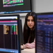 A student is surrounded by Bloomberg terminals, showing data in various colourful representations. 