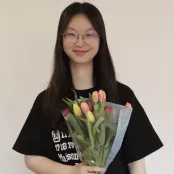 Bin Zhang is smiling at the camera and holding a colourful bunch of tulips.